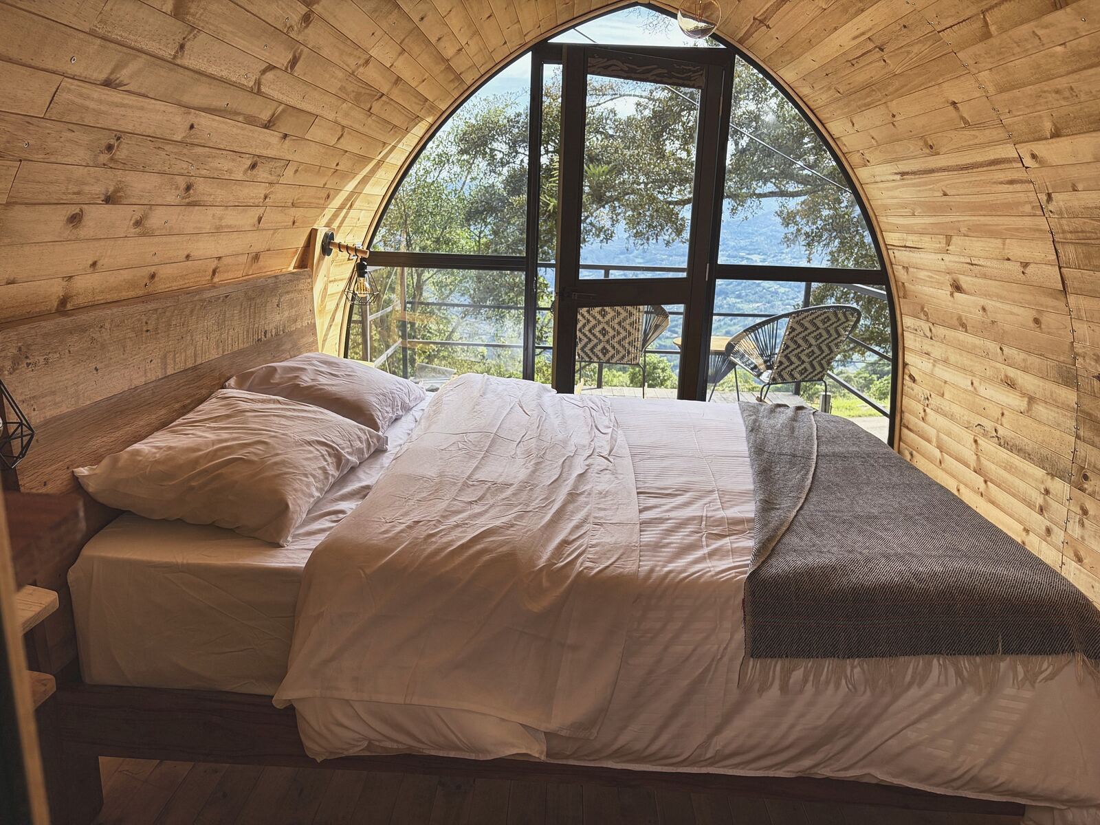 Interior de Alma: la cama queen frente al ventanal en arco que da a la terraza y al bosque